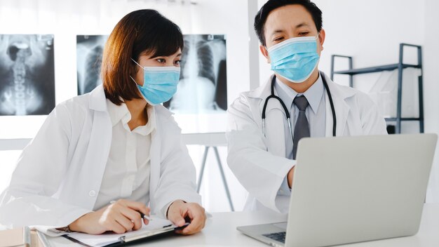 Medical team of asia serious male and young female doctor with protective face masks discussing computed tomography result in hospital office.