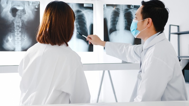 Free photo medical team of asia serious male and young female doctor with protective face masks discussing computed tomography result in hospital office.