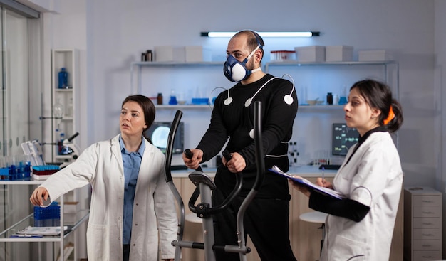 現代​の​実験室​で​の​薬​の​トレーニング中​に​ekg​データ​を​分析する​スポーツマン​の​体​の​持久力​を​監視する​医療​チーム​。​フィットネストレーナー​で​実行されている​電極​センサー​を​持つ​運動​選手​の​男