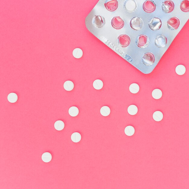 Medical white pills out from the blister pack on pink background