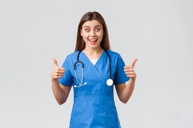 Medical workers, healthcare, covid-19 and vaccination concept. enthusiastic and upbeat female nurse, doctor in blue scrubs, think wonderful idea, show thumbs-up in approval