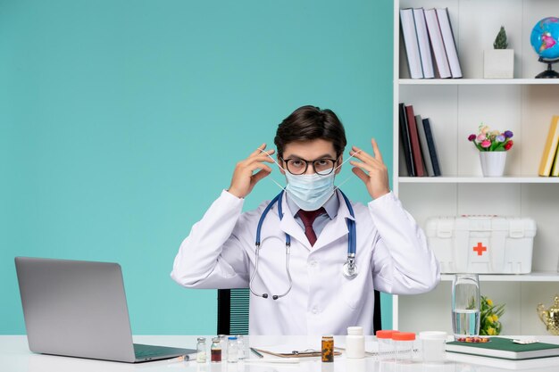 マスクを身に着けている白衣でリモートで深刻なかわいいスマートドクターのコンピューターで働く医療