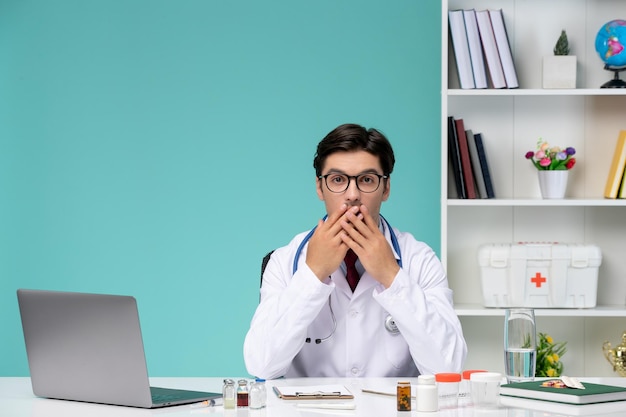 白衣を着た医療の若い賢い医者が、コンピューターに衝撃を与えて口を覆ってリモートで作業している