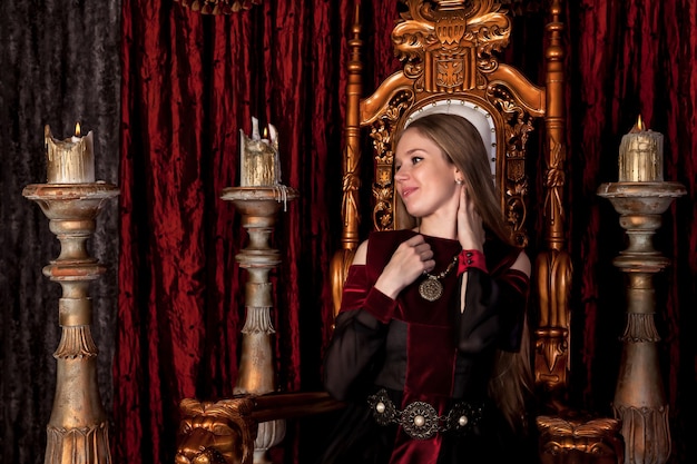 Средневековая королева в историческом наряде на золотом троне в замке. портрет молодой женщины в платье старого стиля на античном троне в приемной крепости. концепция тематических костюмированных мероприятий