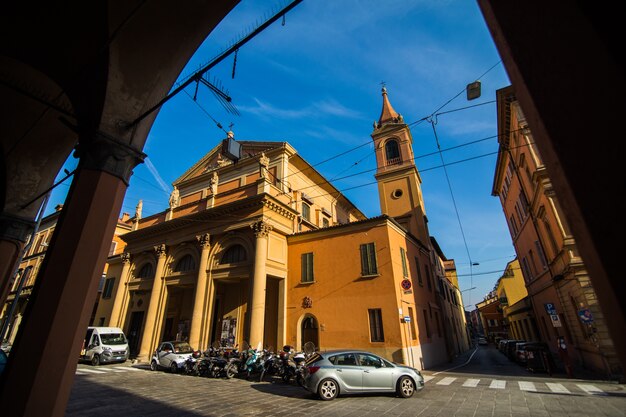 晴れた日の旧市街、ボローニャ、エミリア・ロマーニャ、イタリアの明るい色の家と中世の通りの柱廊玄関