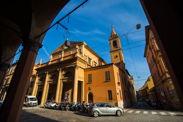 晴れた日の旧市街、ボローニャ、エミリア・ロマーニャ、イタリアの明るい色の家と中世の通りの柱廊玄関