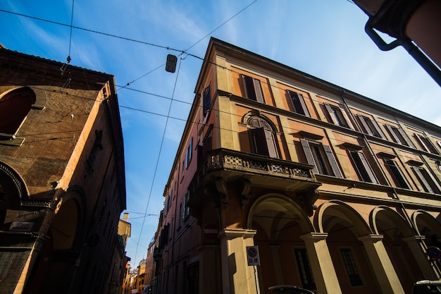 晴れた日の旧市街、ボローニャ、エミリア・ロマーニャ、イタリアの明るい色の家と中世の通りの柱廊玄関