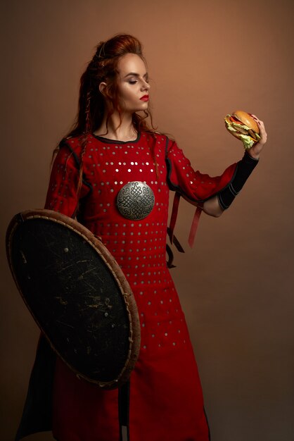 ハンバーガーを保持している中世の戦士がポーズします。