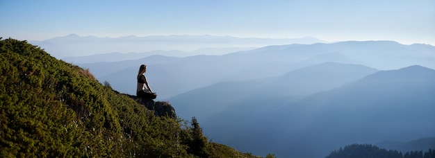 Meditating female is relaxing on in mountains