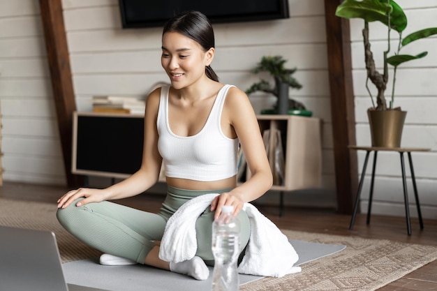 Meditation and online classes concept young woman training remote at home sitting on rubber mat in l...