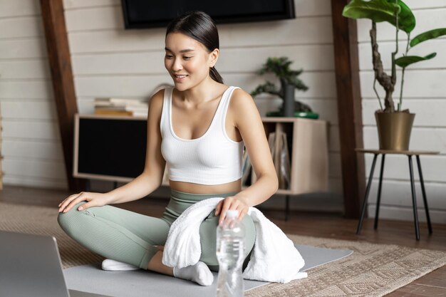 Концепция медитации и онлайн-классов молодая женщина тренируется удаленно дома, сидя на резиновом коврике в л ...