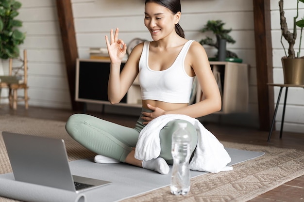 Концепция медитации и онлайн-классов молодая женщина тренируется удаленно дома, сидя на резиновом коврике в л ...