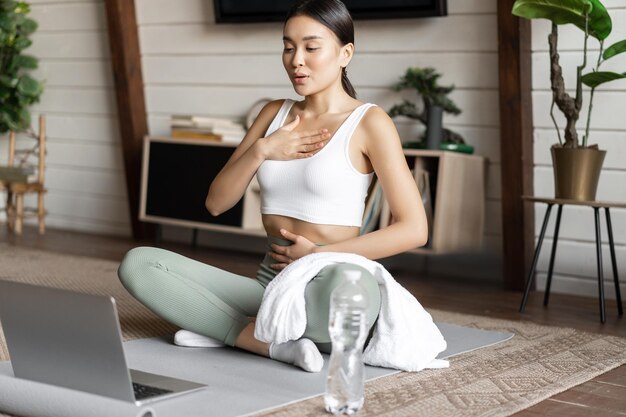 Meditation and online classes concept young woman training remote at home sitting on rubber mat in l...