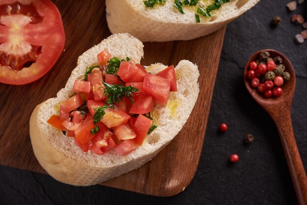 Mediterranean snacks set. Olives, oil, herbs and sliced ciabatta on a wooden board on black slate stone board over dark surface, juicy tomatoes on fresh bread, pesto as topping. top view. Flat lay