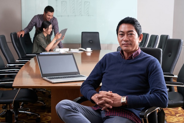 Medium closeup of man in casualwear sitting at the conference table looking at camera