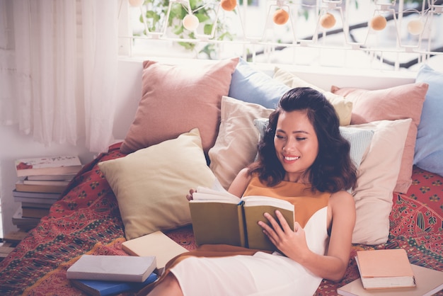Средний крупный план молодой женщины, читающей книгу в ее постели