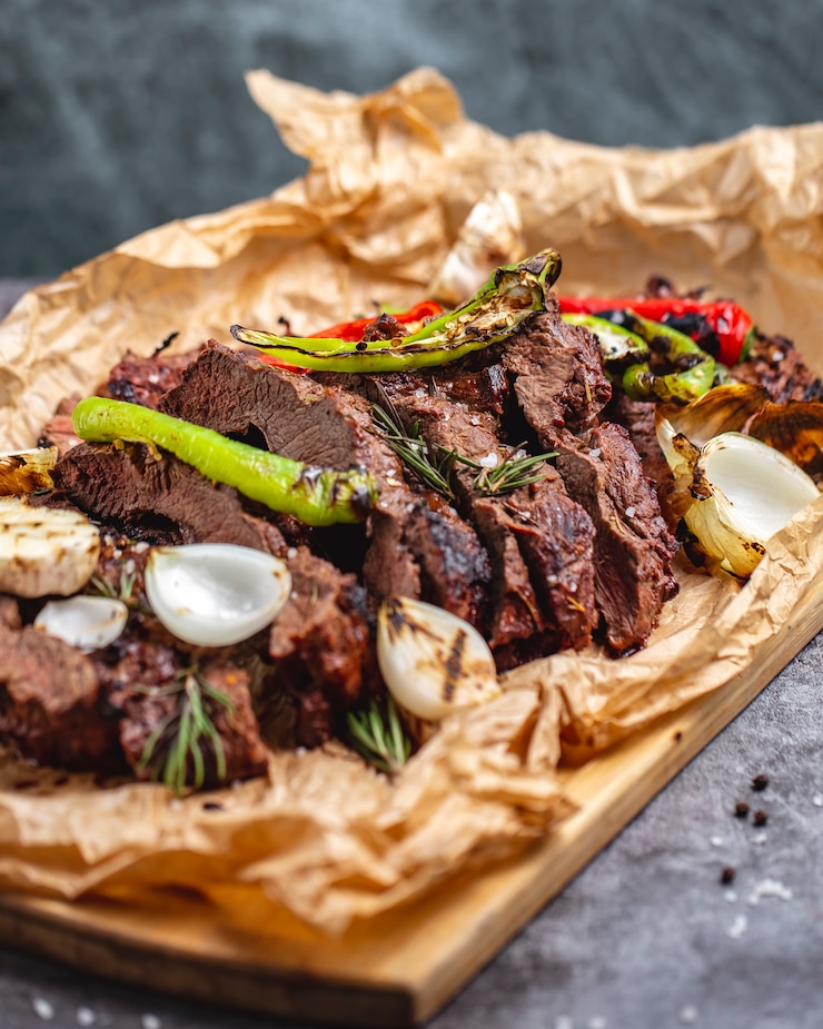 Free Photo medium cooked steak with garlic onion red and chili pepper on parchment paper
