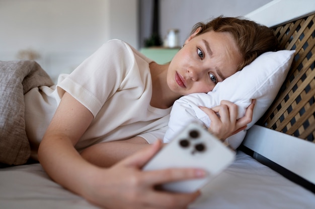 Medium shot anxious woman in bed with phone