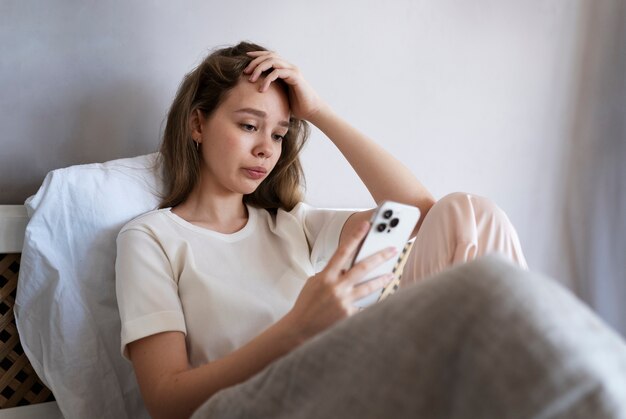 Medium shot anxious woman laying in bed with smartphone