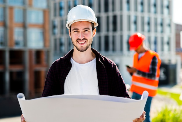 Medium shot of architect holding plans and looking at camera