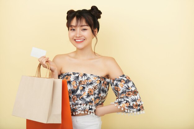 Medium shot of  Asian girl standing with shopping bags and credit card smiling 