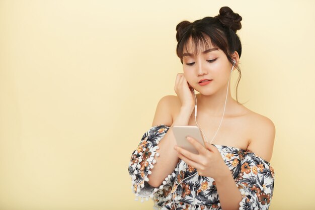 Medium shot of Asian teen girl listening to music on her smartphone