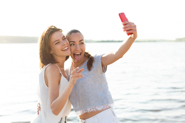 Medium shot beautiful friends taking a selfie next to a lake