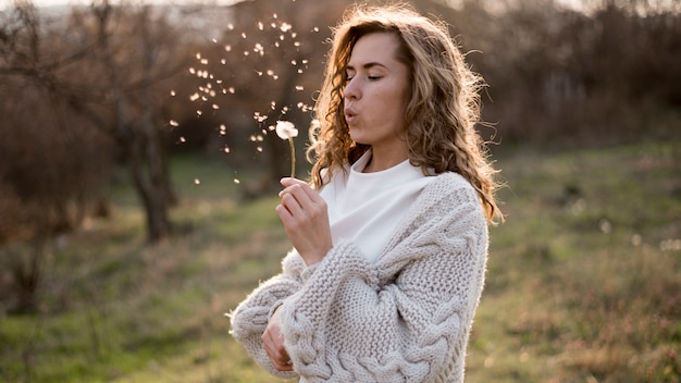 Medium shot of beautiful girl blowing a dandelion