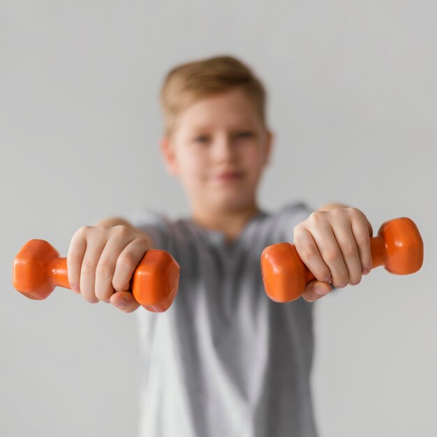 Medium shot blurry kid holding dumbbells