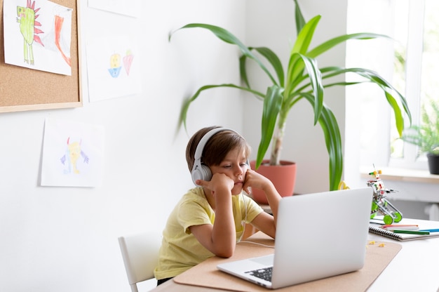 Foto gratuita ragazzo di tiro medio seduto alla scrivania con il computer portatile