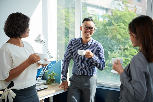 Средний снимок деловых людей, наслаждающихся перерывом на кофе у окна офиса