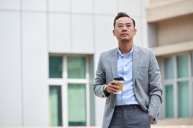 Medium shot of businessman holding the  takeaway coffee and looking forward standing in the street