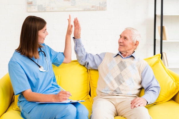 Free photo medium shot caregiver high fiving with old man