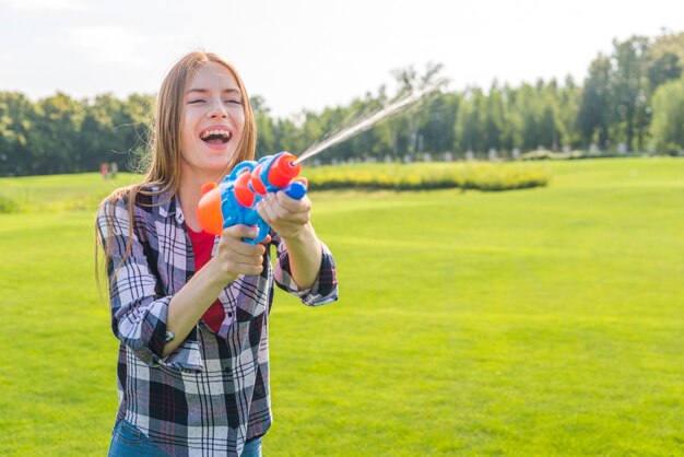 Средний снимок жизнерадостная девушка играет с водяной пушкой