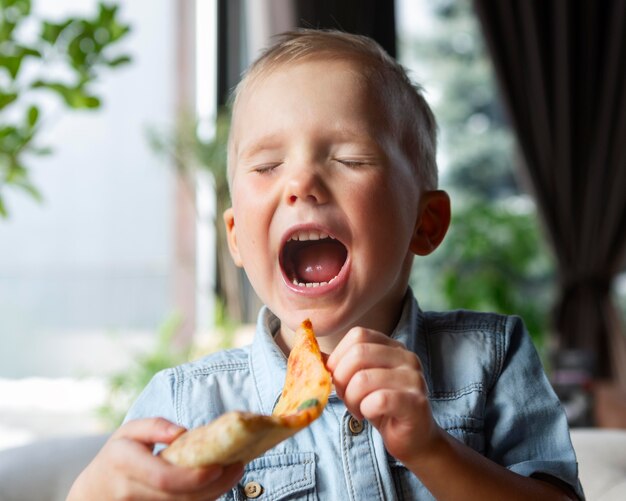 Ребенок среднего выстрела ест кусок пиццы