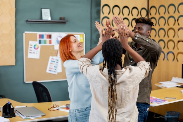 Medium shot colleagues high five at office