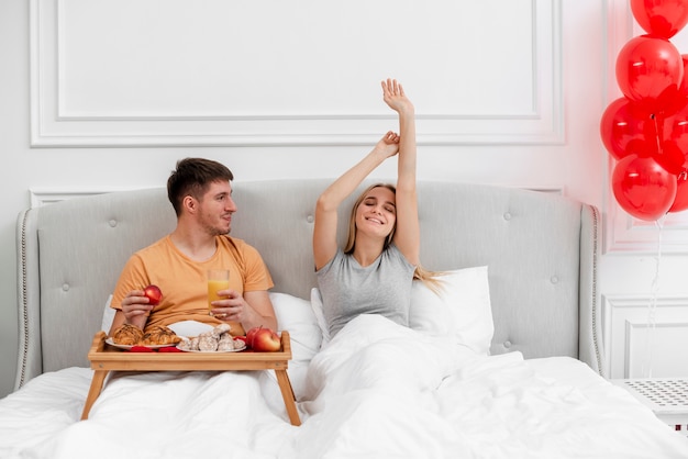 Medium shot couple with breakfast and balloons in bedroom