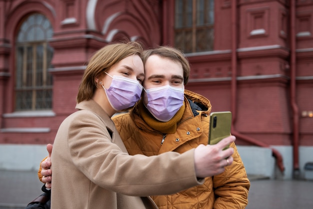 Medium shot couple with masks taking selfie