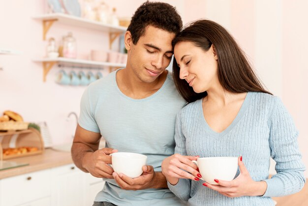 Medium shot couple with mugs in the kitchen