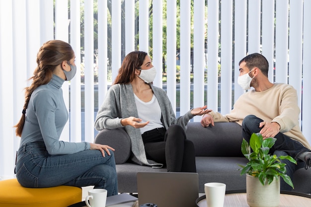 Medium shot coworkers on couch with masks