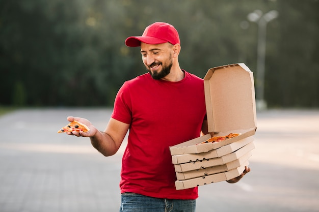 Бесплатное фото Парень с доставкой среднего выстрела смотрит на кусок пиццы