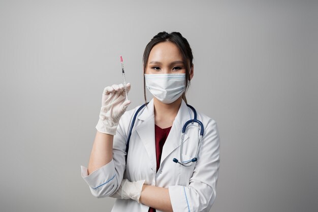 Medico del colpo medio con la maschera che tiene la siringa