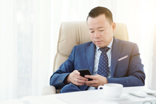 Medium shot of entrepreneur texting a message in his office armchair