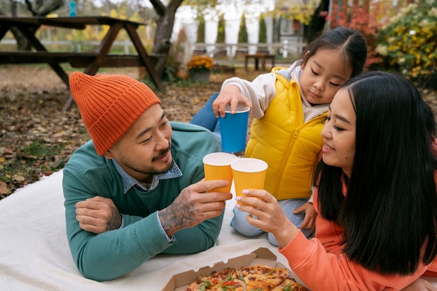 Medium shot family eating pizza outdoors