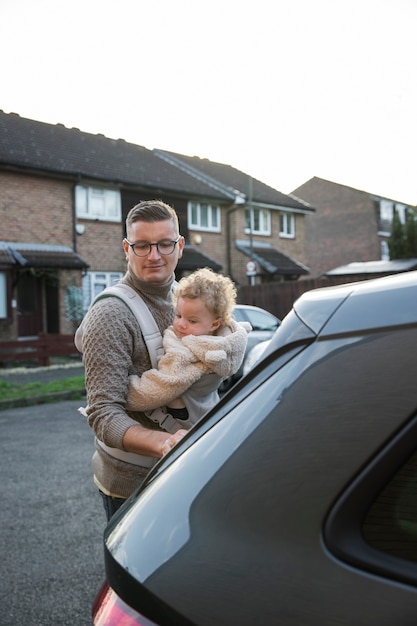 Medium shot father holding baby in carrier