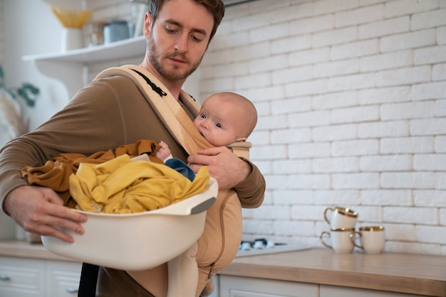 Medium shot father holding baby and doing chores