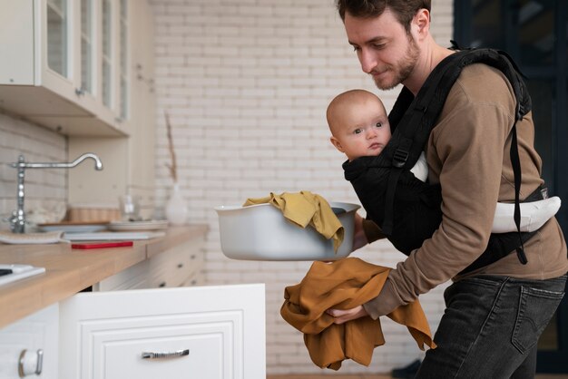 Medium shot father holding baby and doing chores