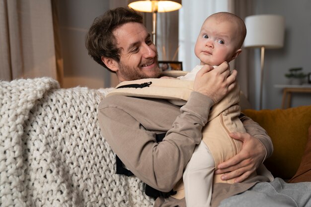 medium shot father holding cute baby in carrier