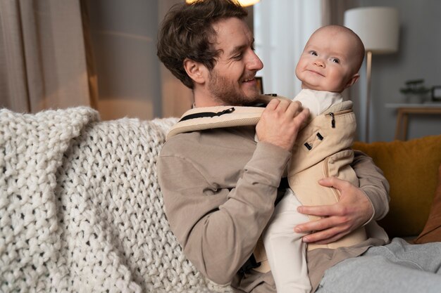 medium shot father holding cute baby in carrier