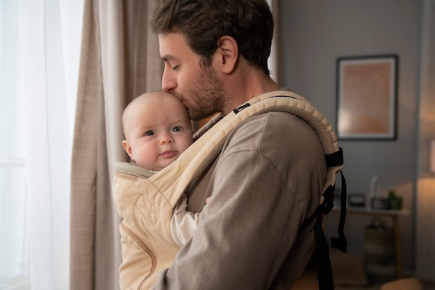Medium shot father holding cute baby in carrier